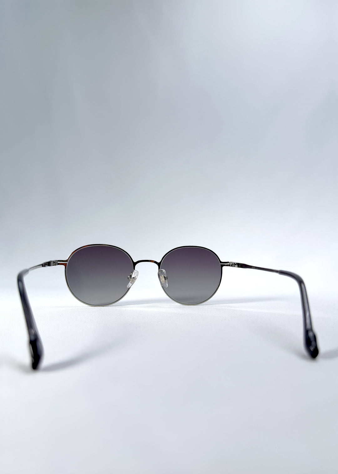 Back view of AZE Liora Arc sunglasses in Moonlit Silver, featuring a silver-tone round frame and gray gradient lenses, showing the inner frame and open temples.