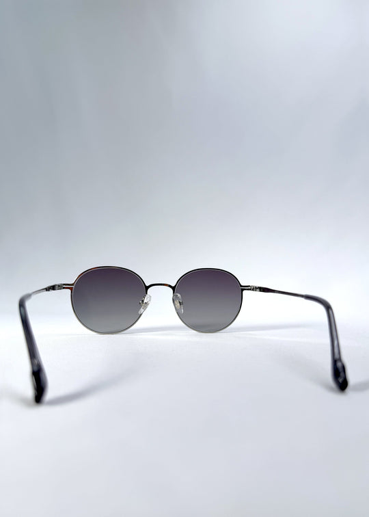 Back view of AZE Liora Arc sunglasses in Moonlit Silver, featuring a silver-tone round frame and gray gradient lenses, showing the inner frame and open temples. 