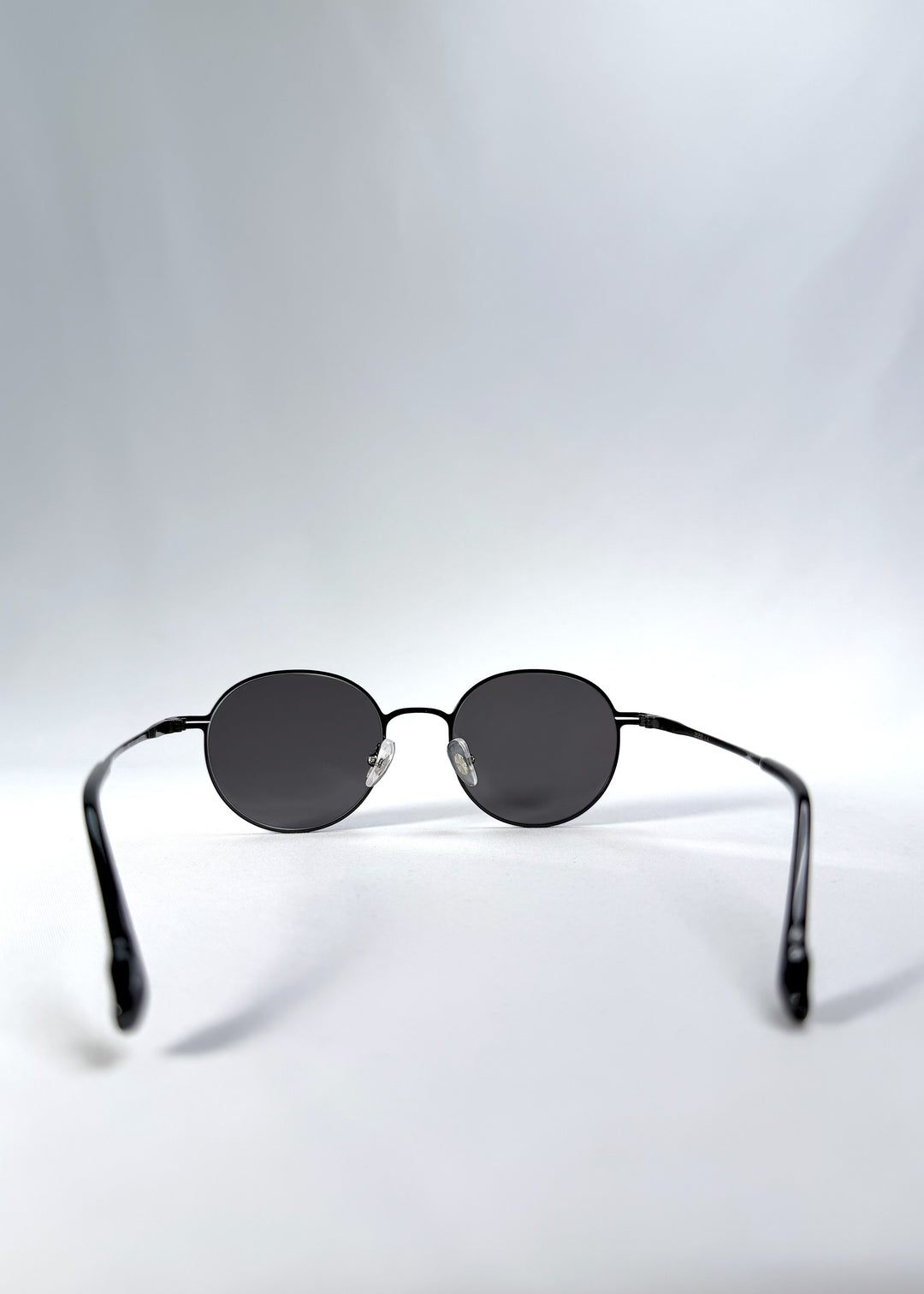 Back view of AZE Liora Arc sunglasses in Obsidian Black, featuring a slim black round frame and smoky gray gradient lenses, showing the inner frame and open temples.