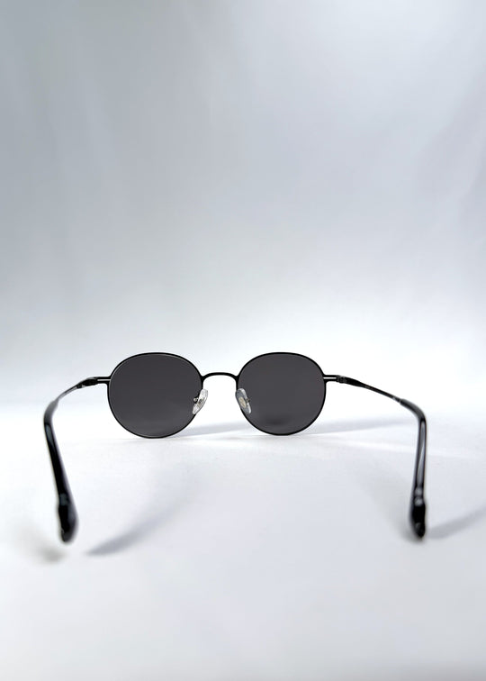 Back view of AZE Liora Arc sunglasses in Obsidian Black, featuring a slim black round frame and smoky gray gradient lenses, showing the inner frame and open temples. 