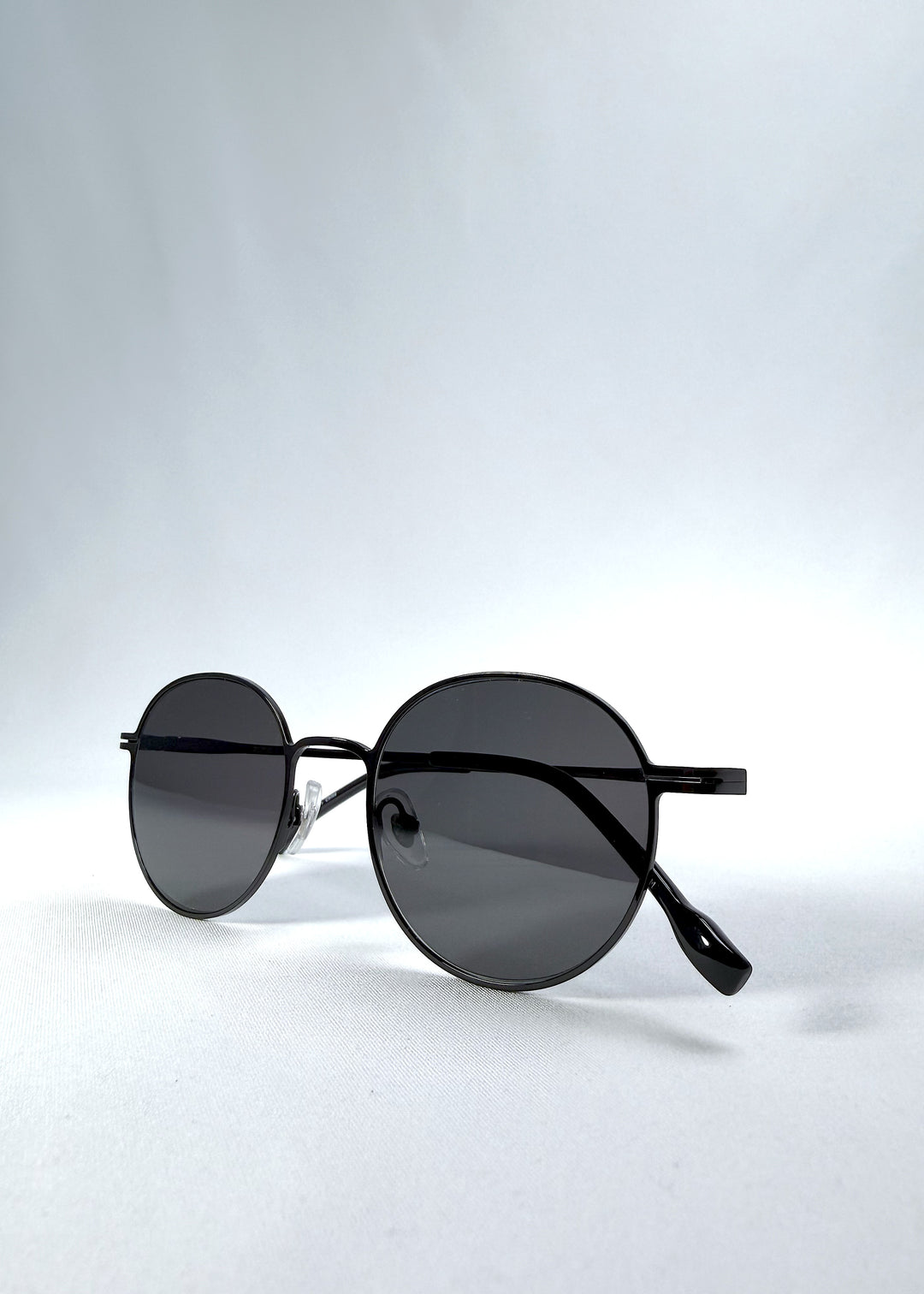 Folded view of AZE Liora Arc sunglasses in Obsidian Black, featuring a slim black round frame and smoky gray gradient lenses, showing the folded temples and frame profile.