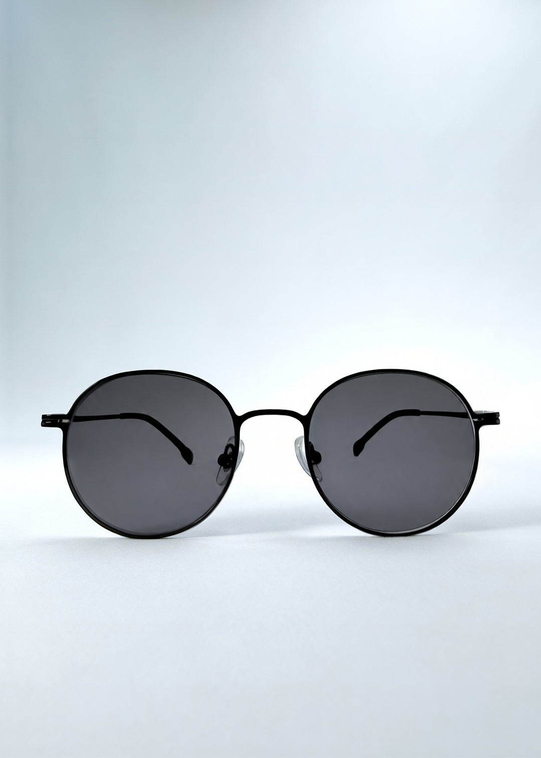 Front view of AZE Liora Arc sunglasses in Obsidian Black, featuring a slim black round frame and smoky gray gradient lenses, showing the full front silhouette.