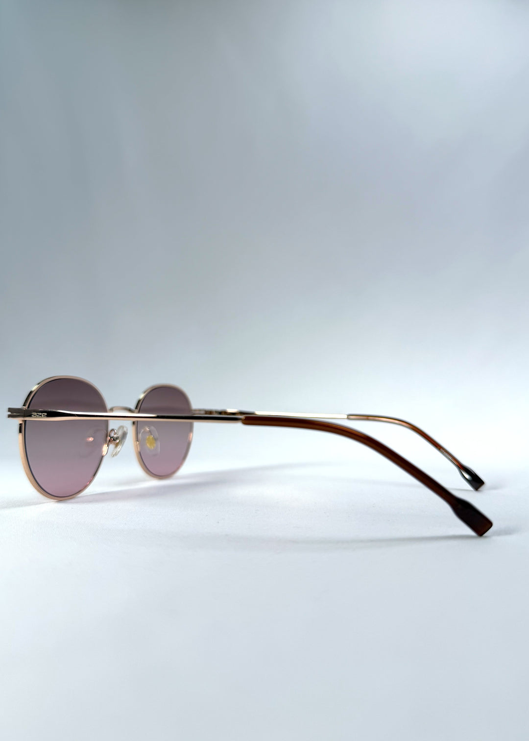 Back-angle view of AZE Liora Arc sunglasses in Rosé Dawn, featuring a rose-gold-tone round frame and soft rose gradient lenses, showing the rear frame structure and temple alignment.