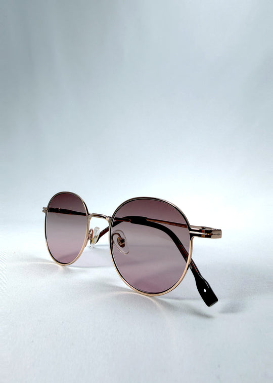 Folded view of AZE Liora Arc sunglasses in Rosé Dawn, featuring a rose-gold-tone round frame and soft rose gradient lenses, showing the folded temples and frame profile.