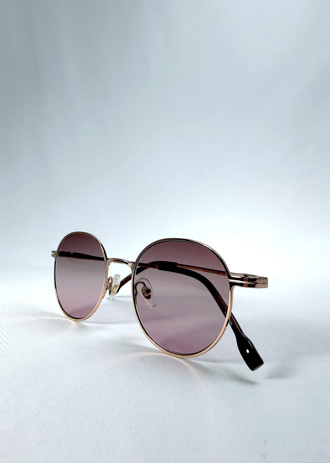 Folded view of AZE Liora Arc sunglasses in Rosé Dawn, featuring a rose-gold-tone round frame and soft rose gradient lenses, showing the folded temples and frame profile. 