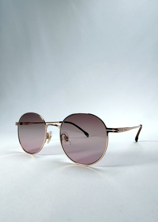 Three-quarter front view of AZE Liora Arc sunglasses in Rosé Dawn, featuring a rose-gold-tone round frame and soft rose gradient lenses, showing the frame shape and temple profile.