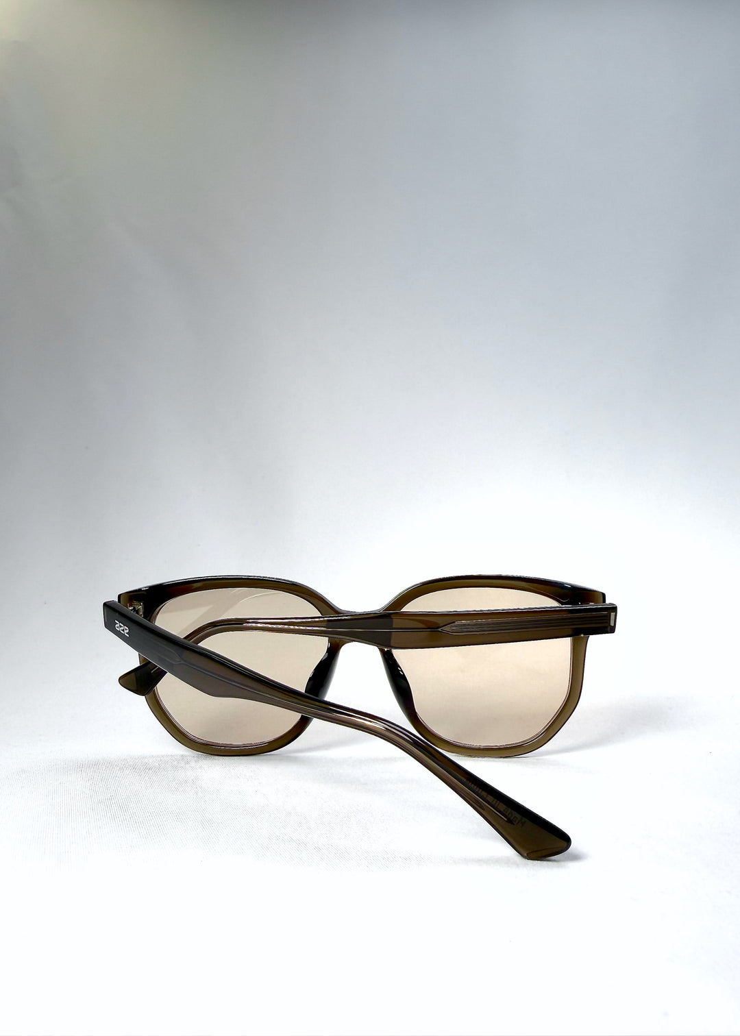 Folded view of Lucent Rift in Sepia Veil with arms crossed over the beige-brown lenses. 