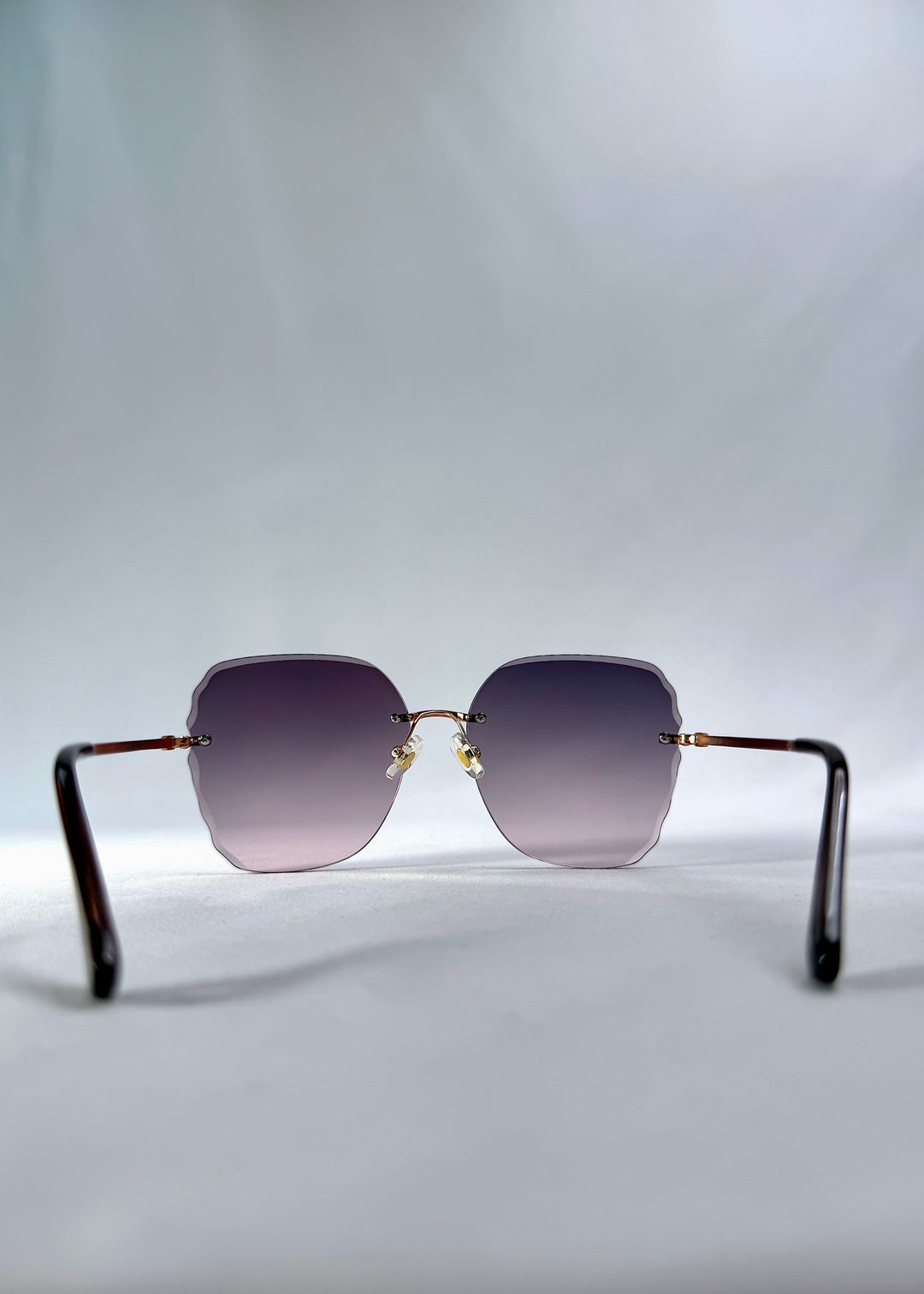 Back view of Lucera sunglasses in Misty Rosé, featuring rimless gold-tone frame and misty rose gradient lenses, showing the inside frame and open temples.
