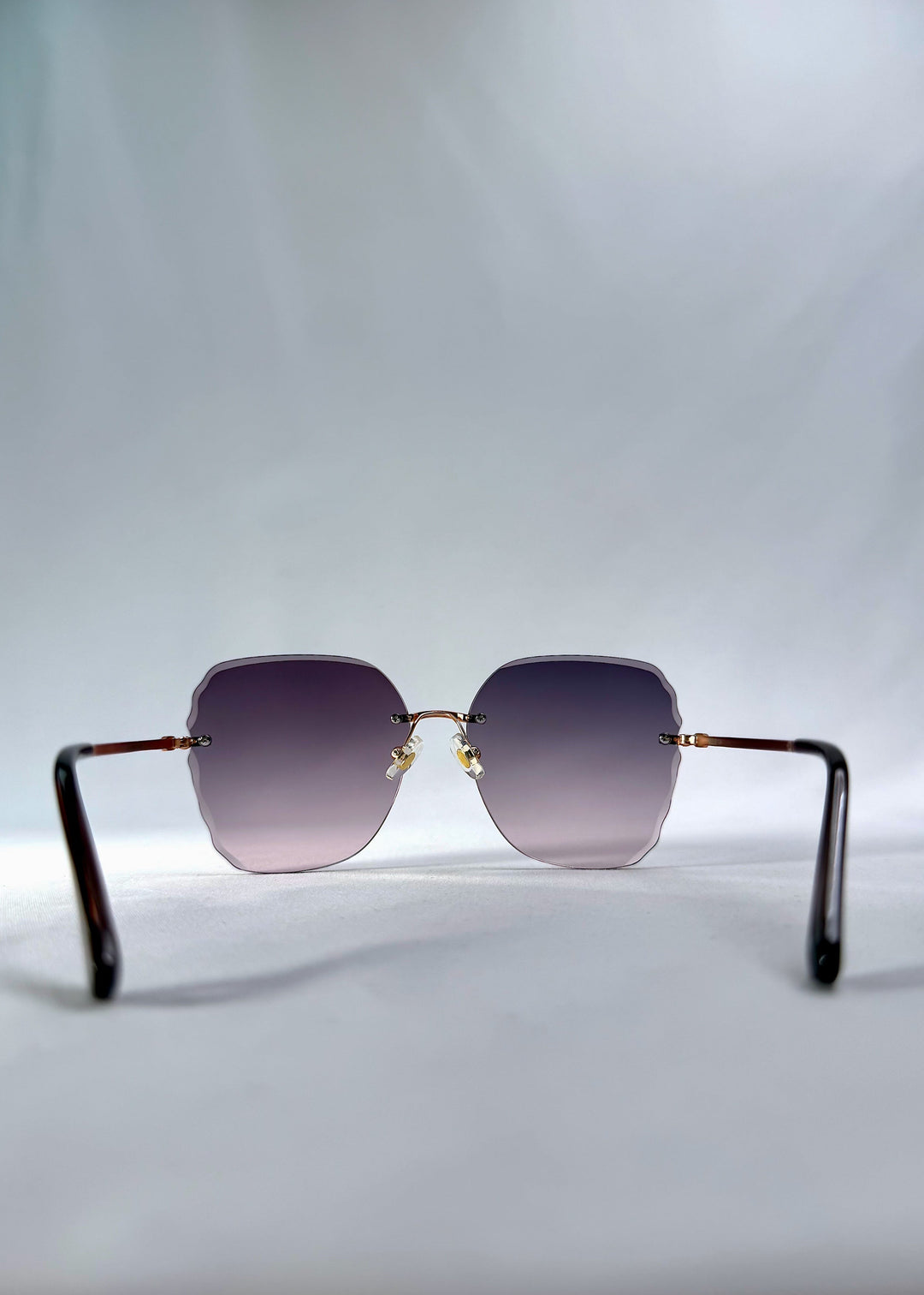 Back view of Lucera sunglasses in Misty Rosé, featuring rimless gold-tone frame and misty rose gradient lenses, showing the inside frame and open temples. 