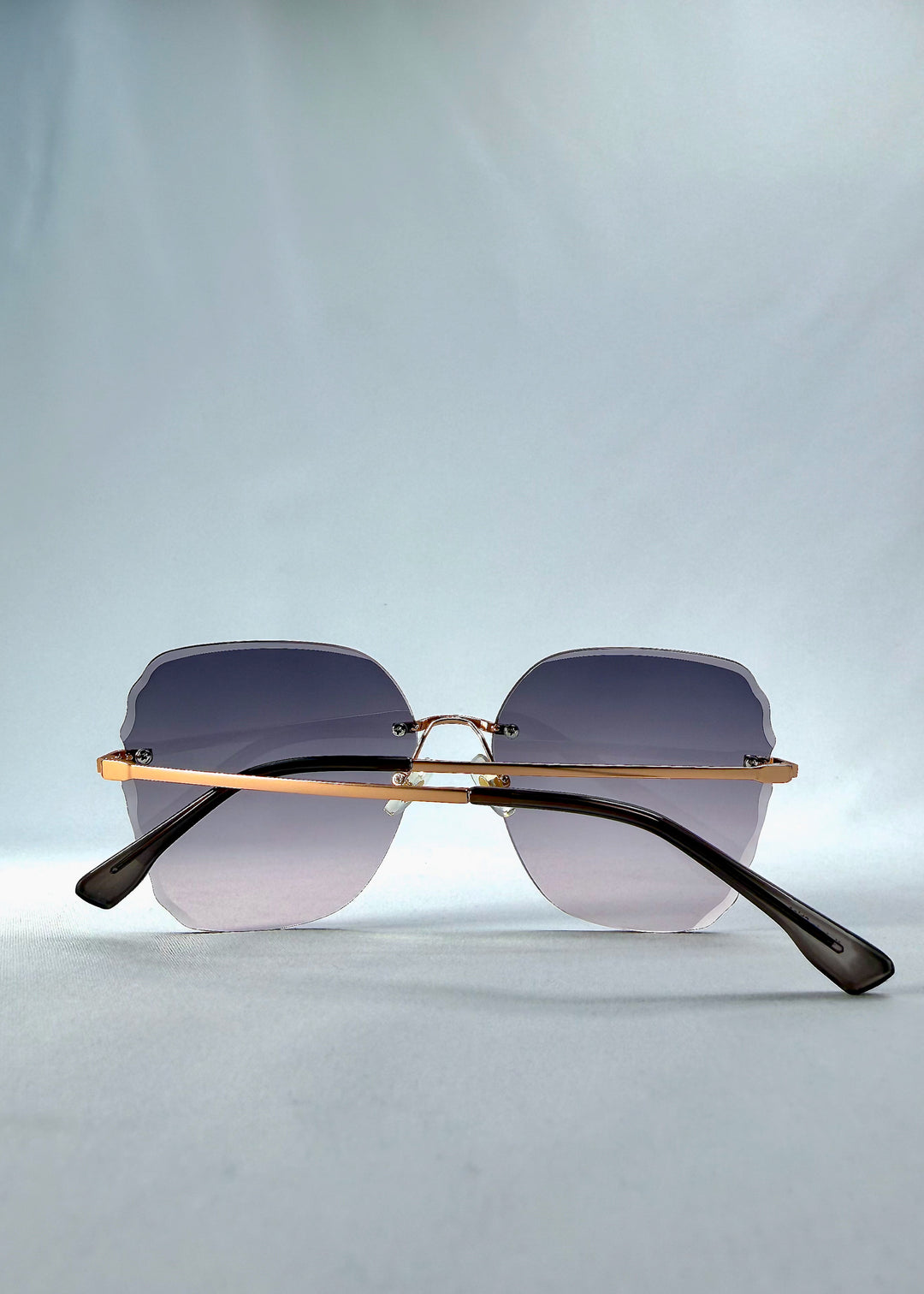 Folded back view of Lucera sunglasses in Misty Rosé, featuring rimless gold-tone frame and misty rose gradient lenses, showing the folded temples and back structure.