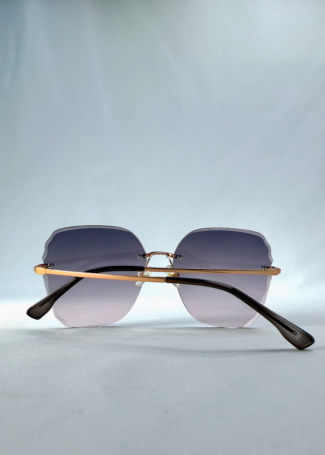 Folded back view of Lucera sunglasses in Misty Rosé, featuring rimless gold-tone frame and misty rose gradient lenses, showing the folded temples and back structure. 