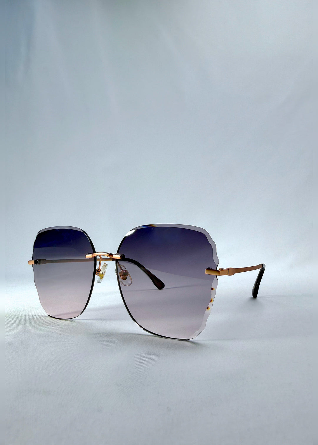 Three-quarter front view of Lucera sunglasses in Misty Rosé, featuring rimless gold-tone frame and misty rose gradient lenses, showing the front shape and temple profile. 