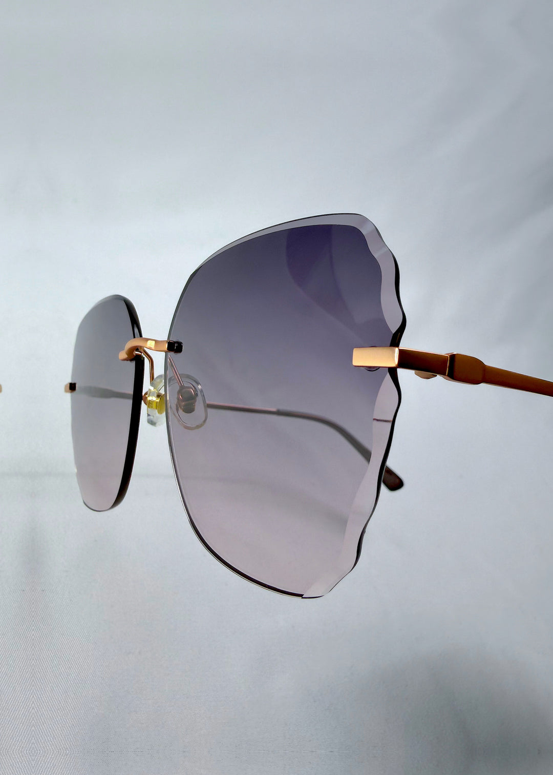 Close-up hinge detail view of Lucera sunglasses in Misty Rosé, featuring rimless gold-tone frame and misty rose gradient lenses, showing the hinge, lens edge, and temple detail.