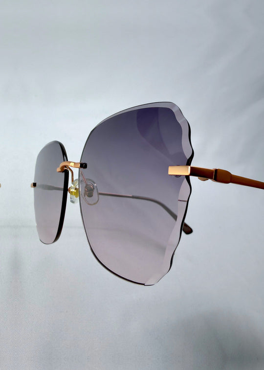 Close-up hinge detail view of Lucera sunglasses in Misty Rosé, featuring rimless gold-tone frame and misty rose gradient lenses, showing the hinge, lens edge, and temple detail. 