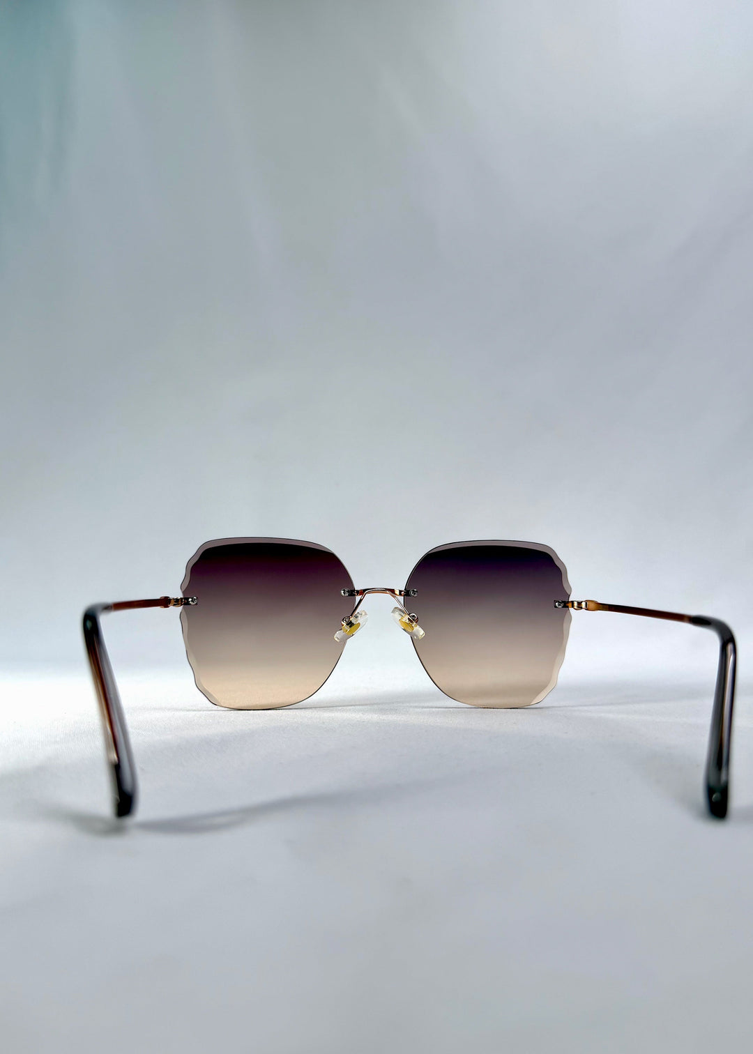 Back view of Lucera sunglasses in Taupe Veil, featuring rimless gold-tone frame and taupe gradient lenses, showing the inside frame and open temples. 