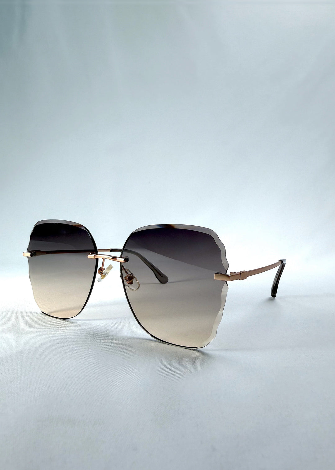 Three-quarter front view of Lucera sunglasses in Taupe Veil, featuring rimless gold-tone frame and taupe gradient lenses, showing the front shape and temple profile. 