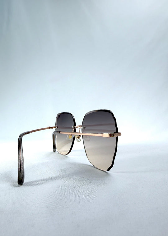 Close-up side detail view of Lucera sunglasses in Taupe Veil, featuring rimless gold-tone frame and taupe gradient lenses, showing the side lens edge, hinge, and temple detail. 
