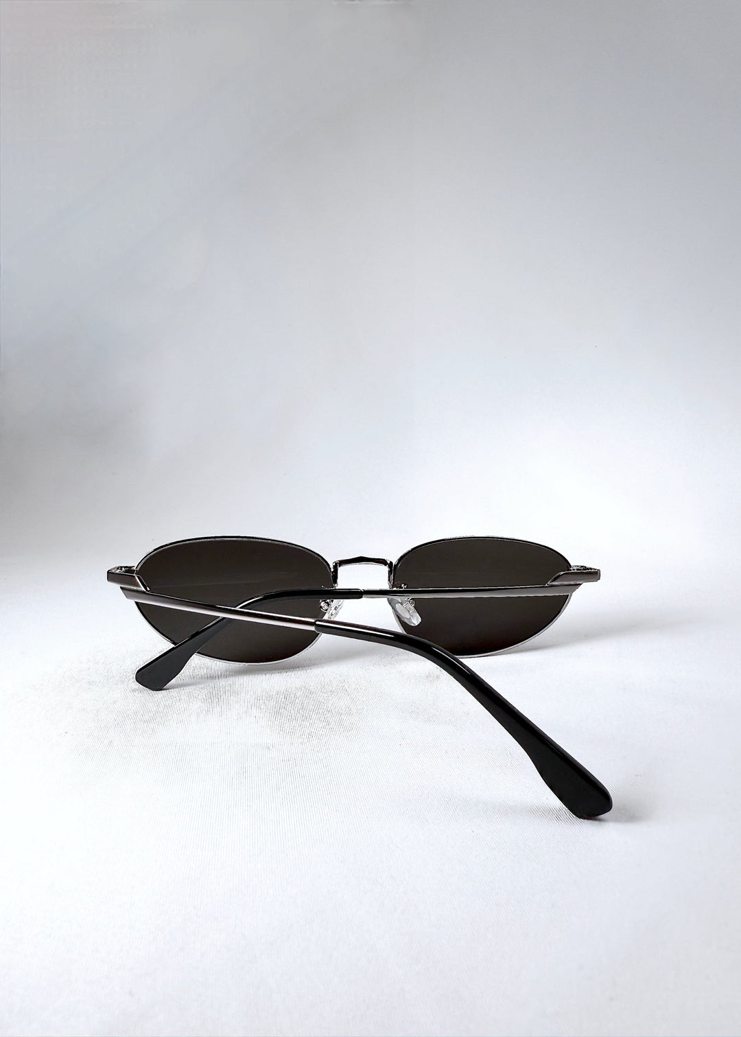 Back view of Lunaris - Moonlit Silver sunglasses in a folded position, with temples crossed over the silver frame. 