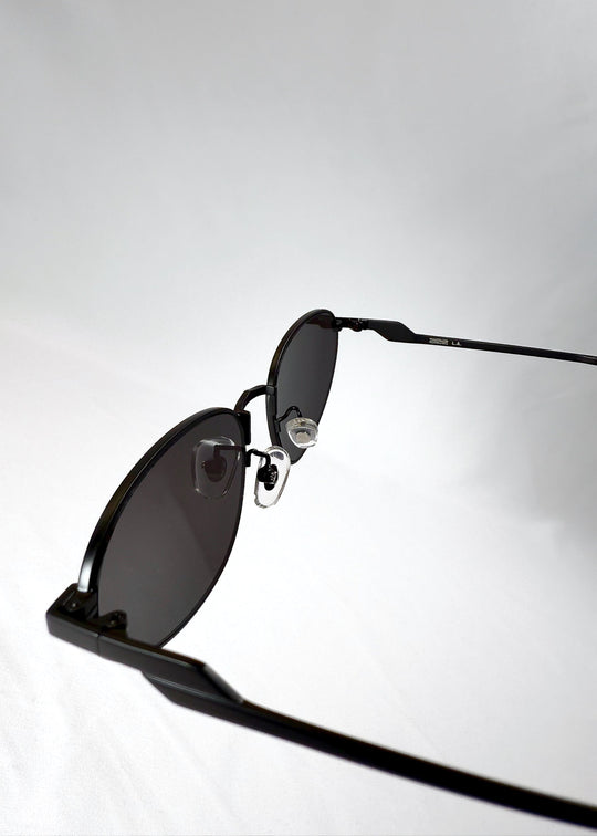 Closeup view of Lunaris - Shadow Black sunglasses showcasing the adjustable nose pads and precision hinge detailing on the matte black metal frame. 
