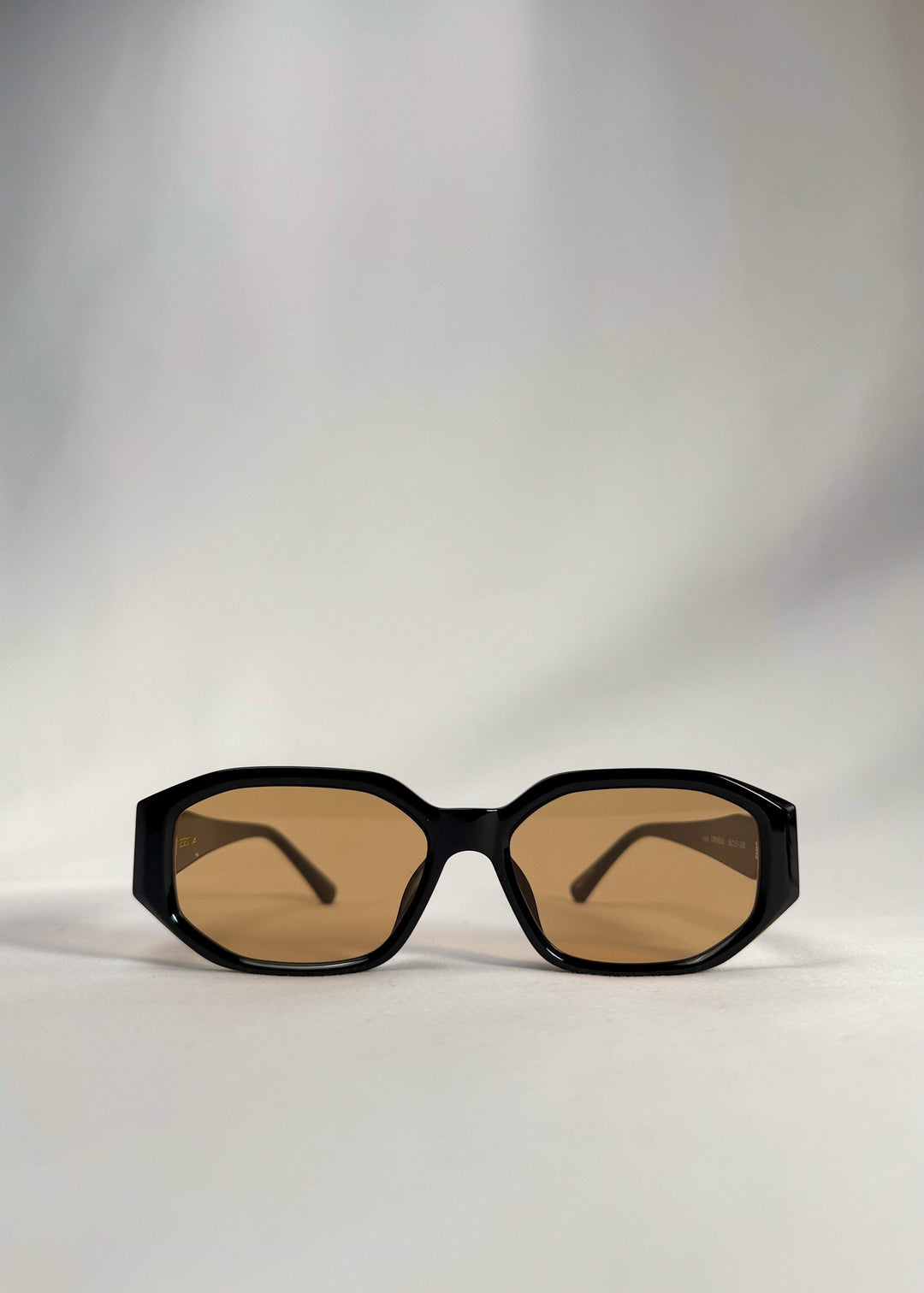 Front view of Lyra sunglasses in Amber, featuring a glossy black acetate frame with amber-tinted lenses, showing the full front silhouette. 