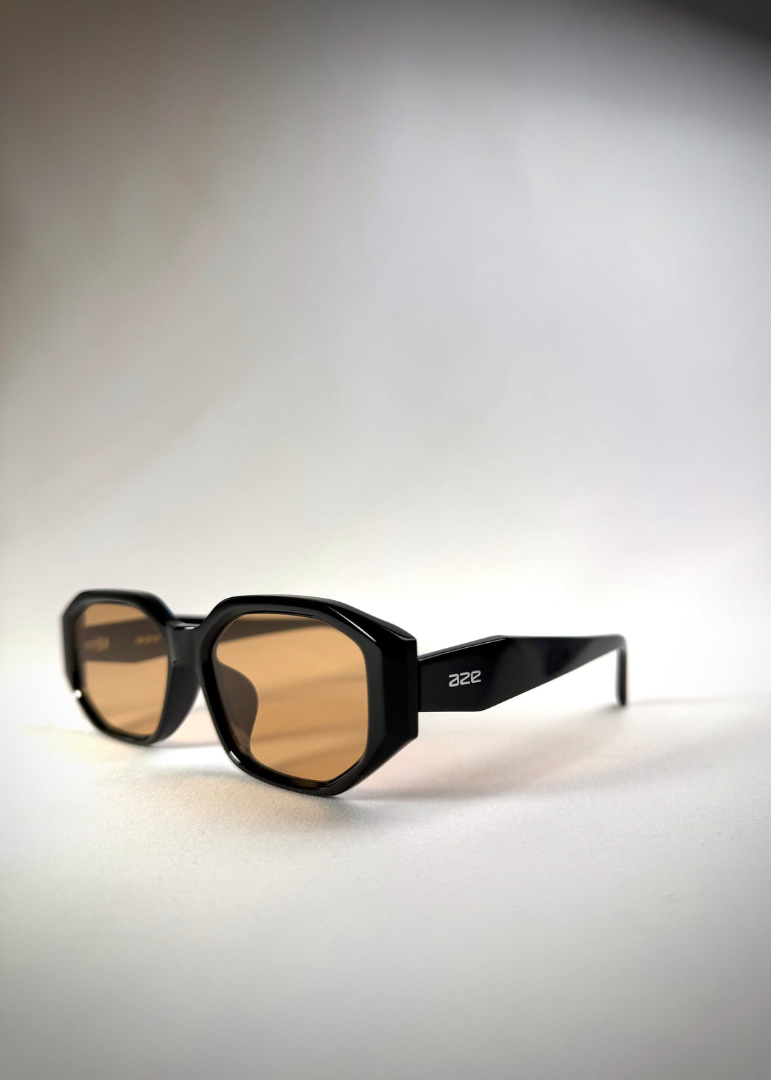 Three-quarter side view of Lyra sunglasses in Amber, featuring a glossy black acetate frame with amber-tinted lenses, showing the frame contours and lens tint. 