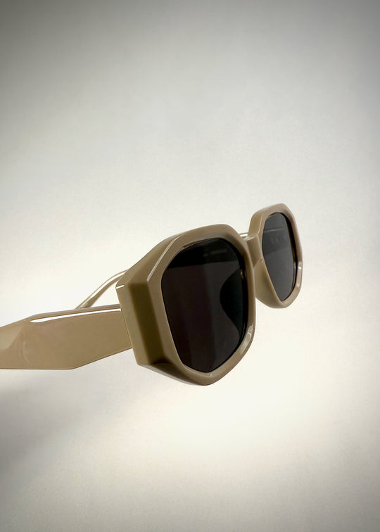 Angled view of Lyra sunglasses in Creamy Beige, featuring a sculpted acetate frame, angular lens shape, and UV400 lenses, showing the geometric frame structure. 
