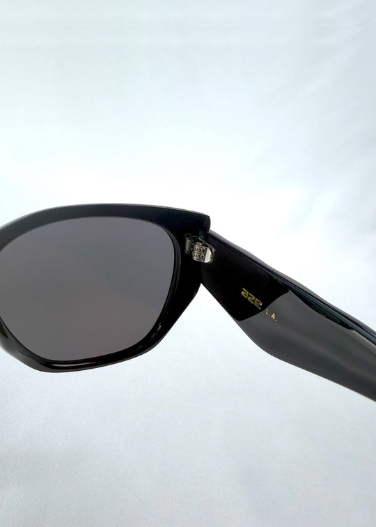 Close-up hinge detail view of Marlowe sunglasses in Obsidian Black, featuring glossy black acetate frame and dark lenses, showing the hinge, lens edge, and temple detail. 