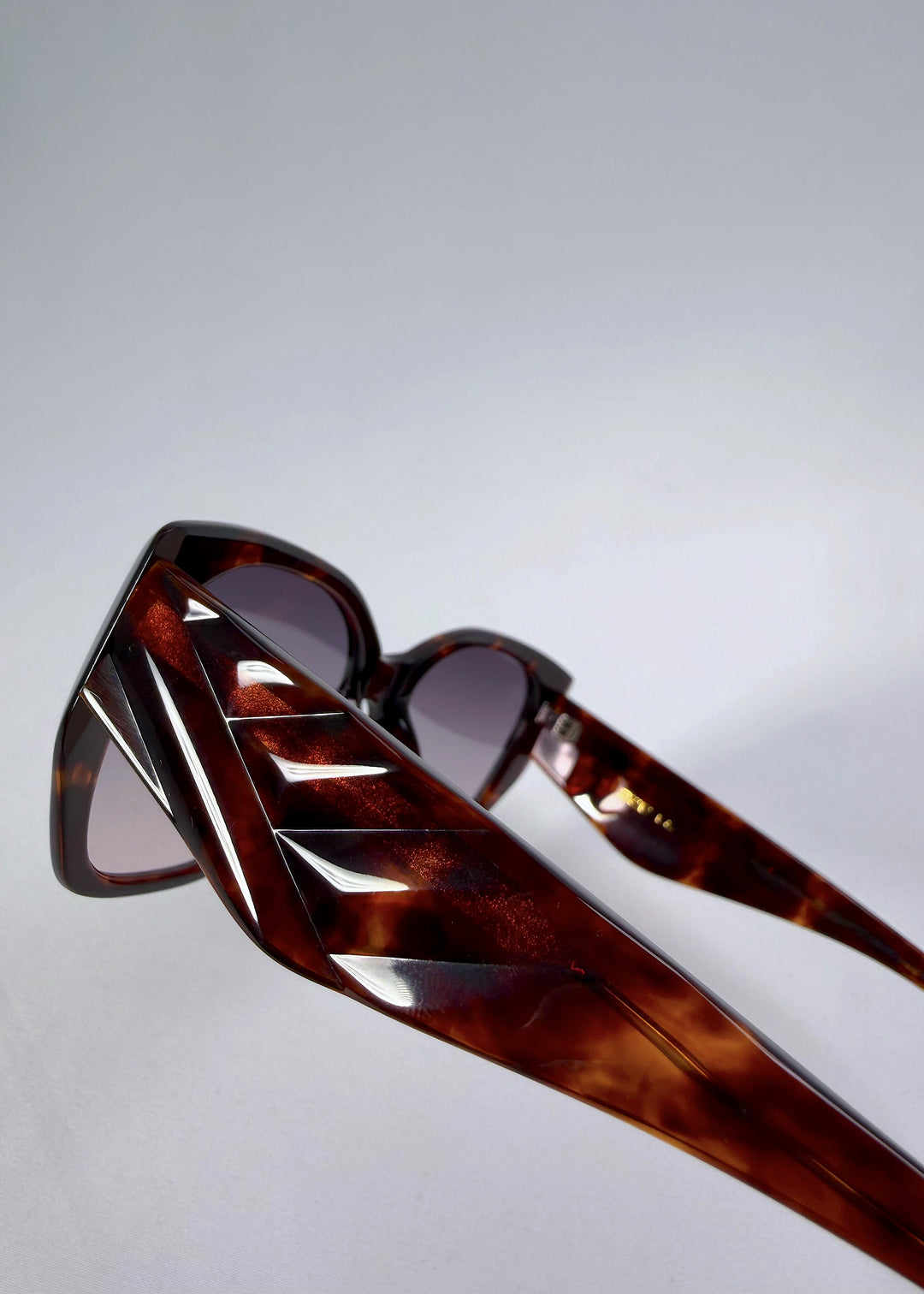 Close-up hinge detail view of Marlowe sunglasses in Tortoiseshell, featuring a sculpted tortoiseshell acetate frame and smoky gradient lenses, showing the hinge construction, lens edge, and temple connection.