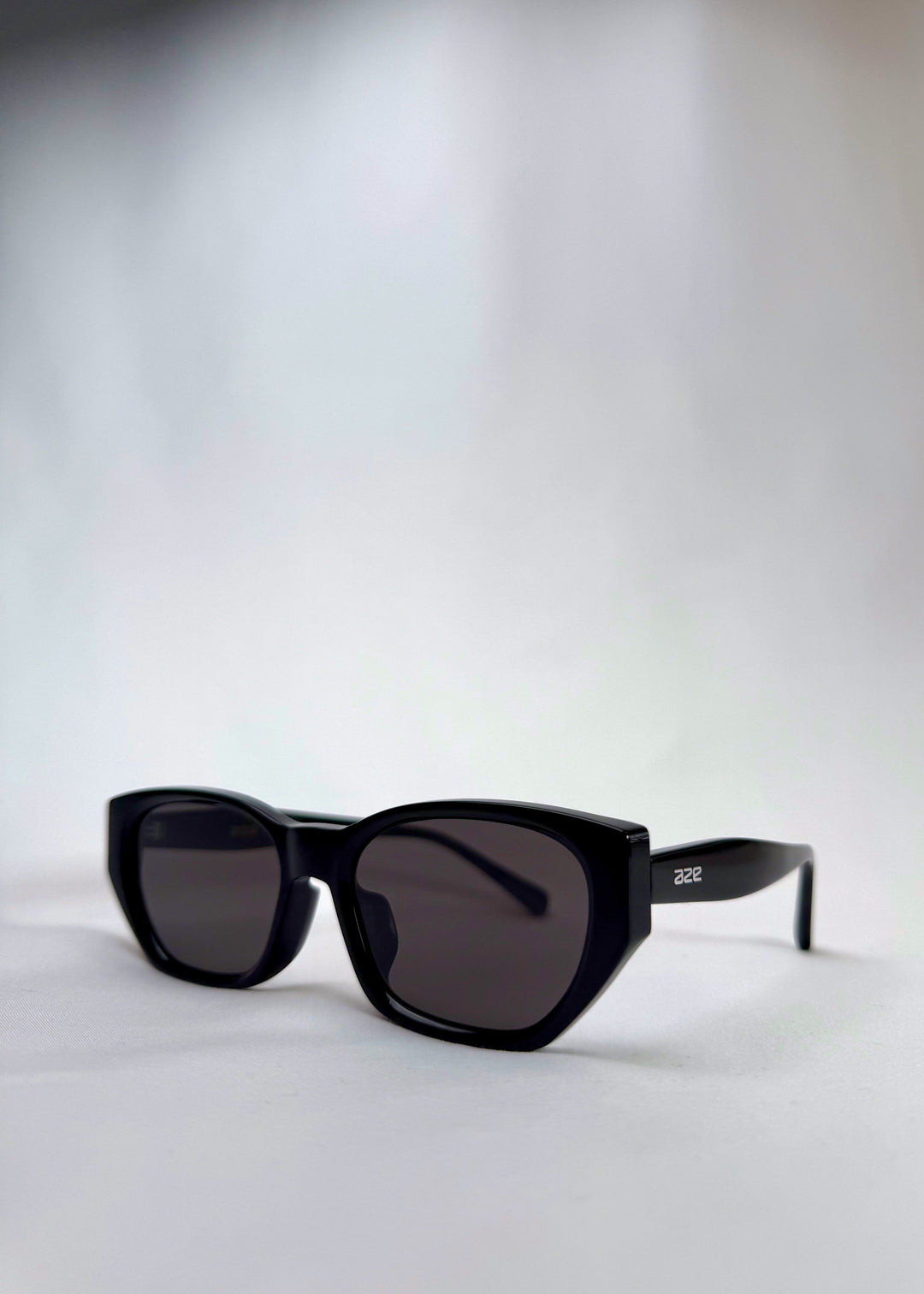 Three-quarter front view of Mirach sunglasses in Black, featuring a glossy black acetate frame and gray UV400 lenses, showing the front shape and temple profile. 
