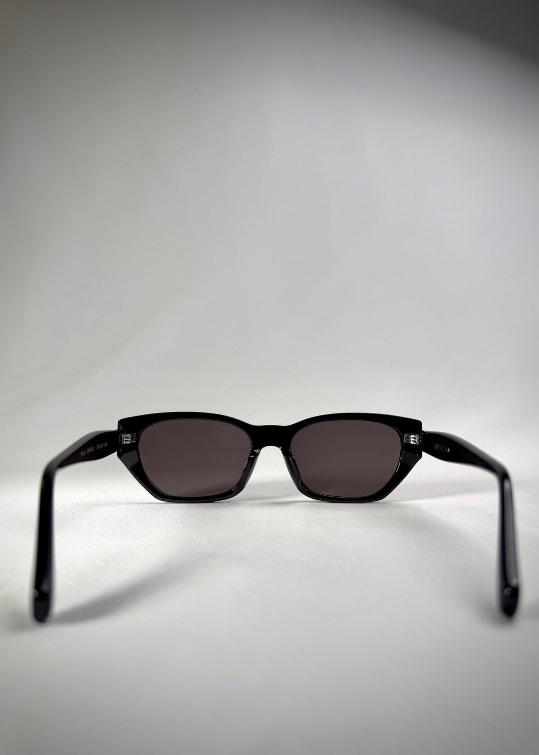 Back view of Mirach sunglasses in Black, featuring a glossy black acetate frame and gray UV400 lenses, showing the inside frame and open temples. 