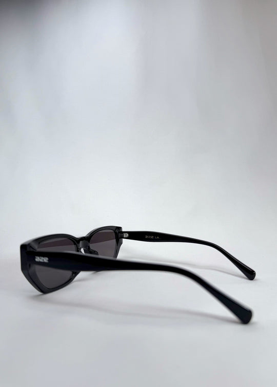 Side-angle view of Mirach sunglasses in Black, featuring a glossy black acetate frame and gray UV400 lenses, showing the lens shape and temple profile. 