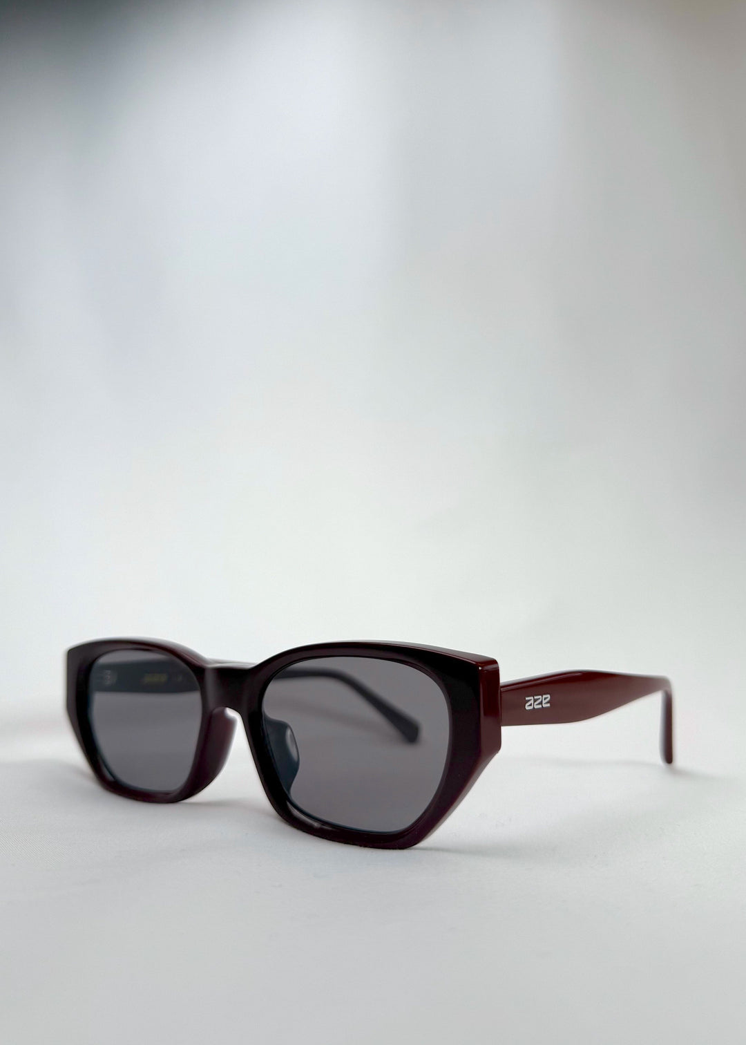 Three-quarter side view of Mirach sunglasses in Burgundy, featuring a deep burgundy acetate frame and gray UV400 lenses, showing the front shape and temple profile. 