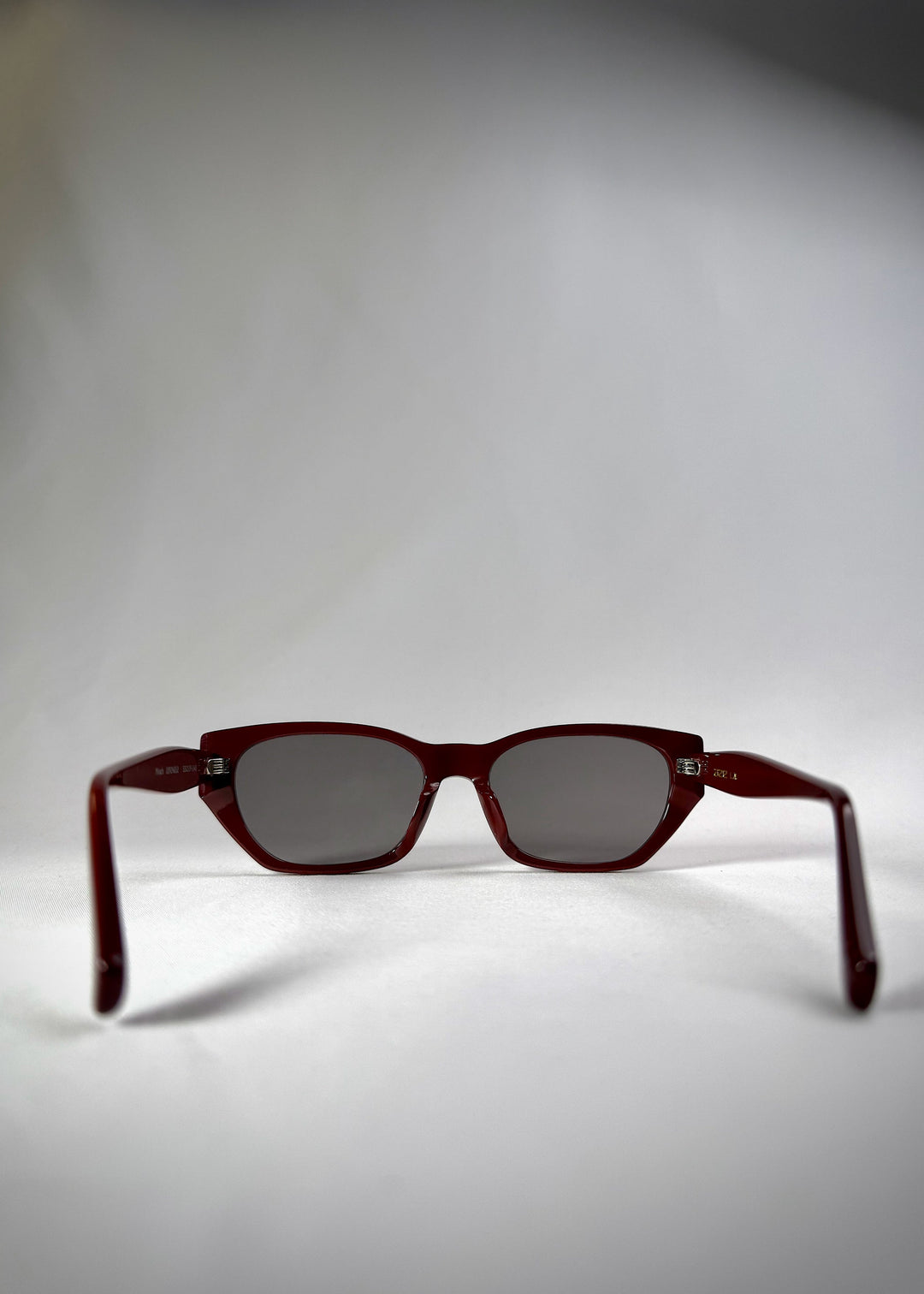 Back view of Mirach sunglasses in Burgundy, featuring a deep burgundy acetate frame and gray UV400 lenses, showing the inside frame and open temples. 