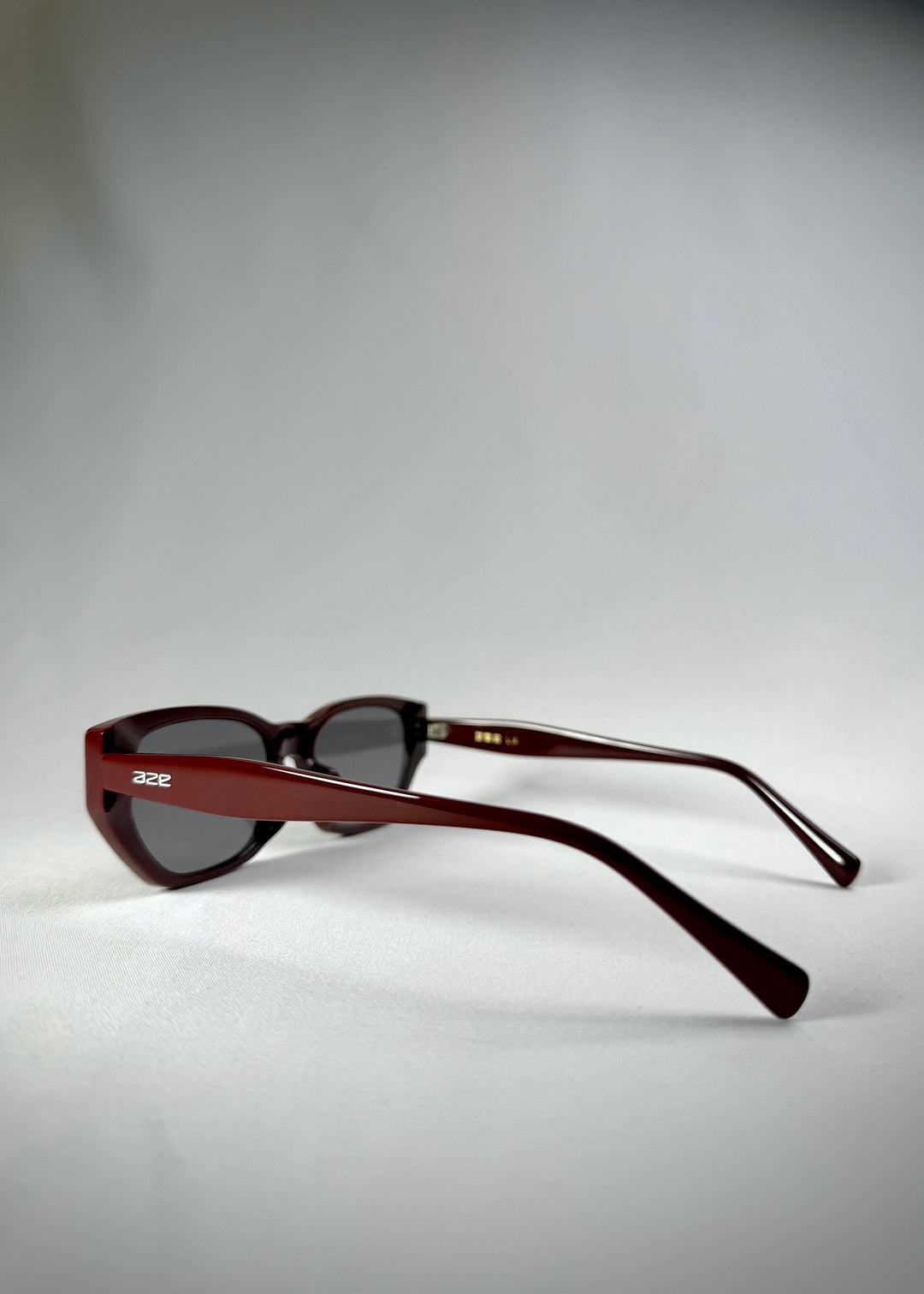 Side-angle view of Mirach sunglasses in Burgundy, featuring a deep burgundy acetate frame and gray UV400 lenses, showing the lens shape and temple profile. 