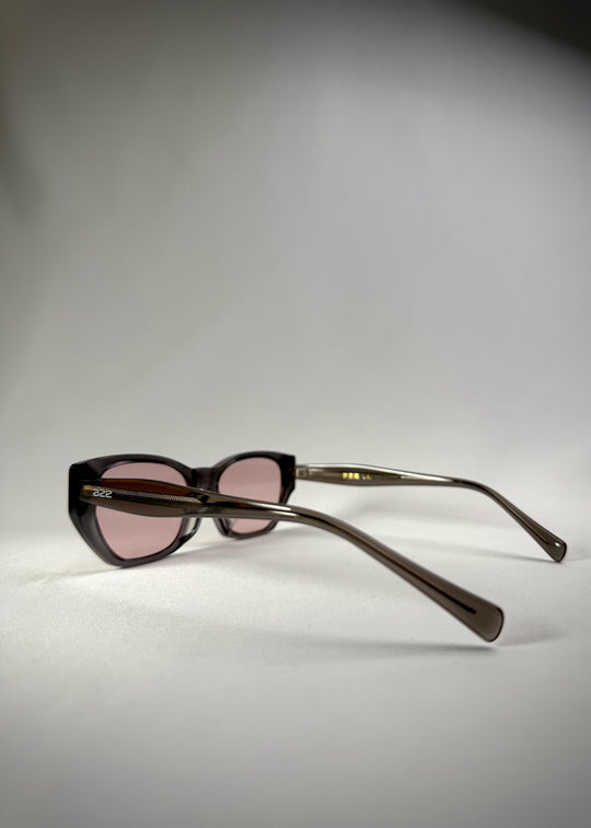 Back-angle view of Mirach sunglasses in Transparent Gray, featuring a smoke-gray translucent acetate frame and pink-tinted lenses, showing the back structure and tapered temples. 