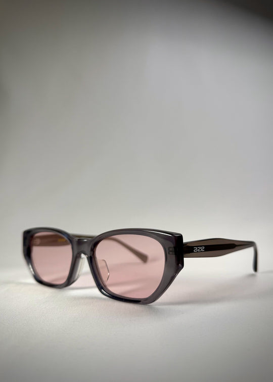 Side-angle view of Mirach sunglasses in Transparent Gray, featuring a smoke-gray translucent acetate frame and pink-tinted lenses, showing the lens shape and temple profile. 