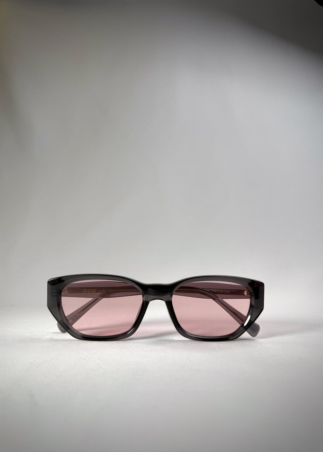 Folded view of Mirach sunglasses in Transparent Gray, featuring a smoke-gray translucent acetate frame and pink-tinted lenses, showing the folded temples and frame profile. 