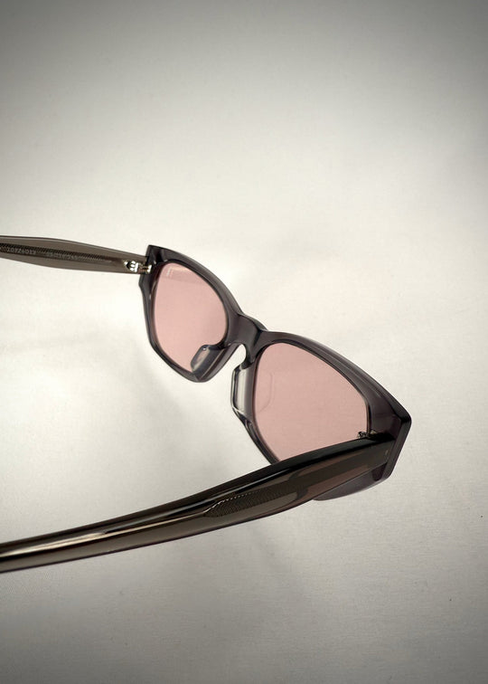 Rear view of Mirach sunglasses in Transparent Gray, featuring a smoke-gray translucent acetate frame and pink-tinted lenses, showing the inside frame and extended temples. 