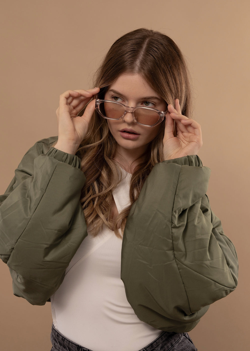 Female model in olive jacket wearing Mirach Transparent White prescription sunglasses – effortlessly blending style and sophistication.