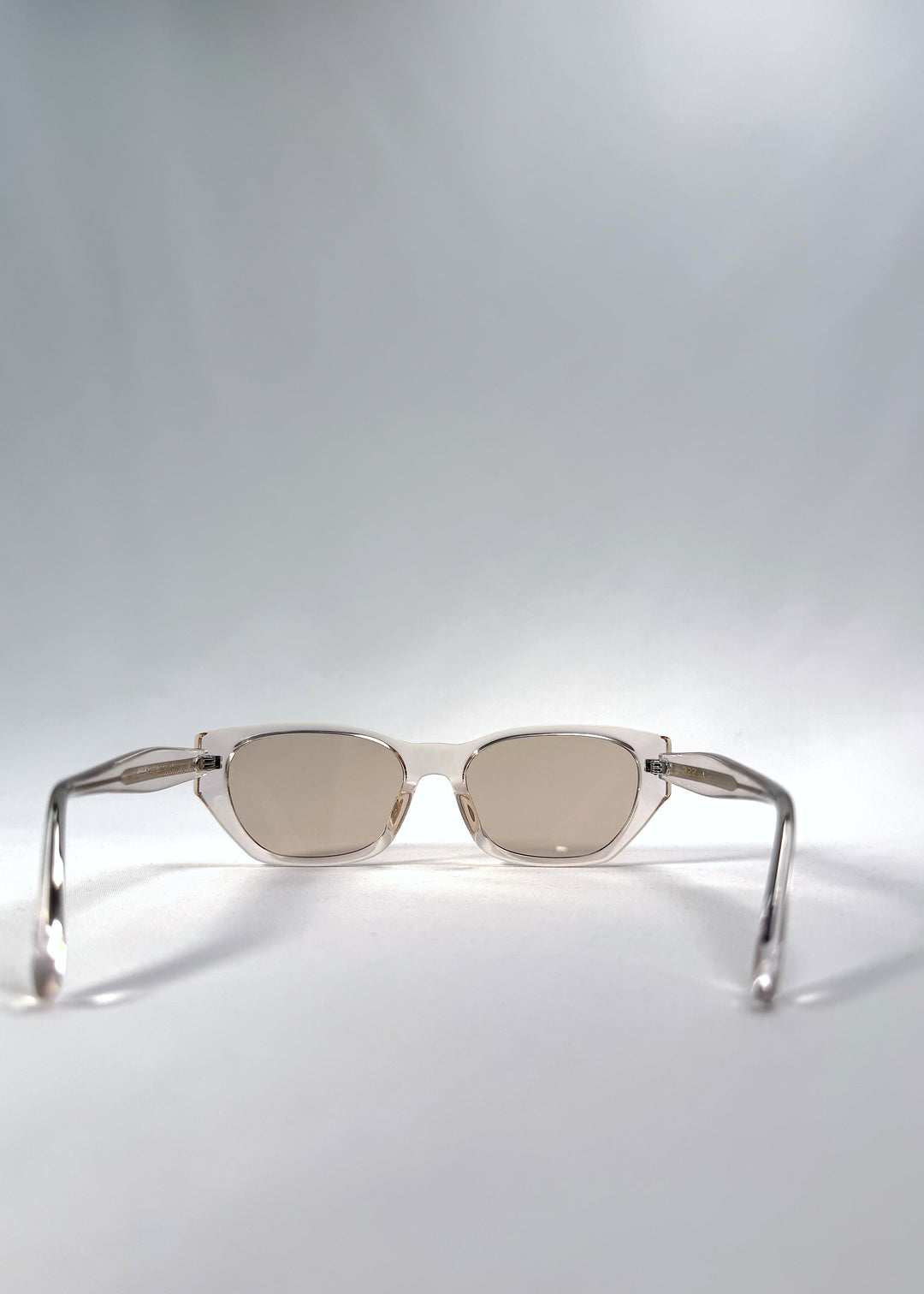 Back view of Mirach sunglasses in Transparent White, featuring crystal-clear acetate frame and tea-tinted lenses, showing the inside frame and open temples.