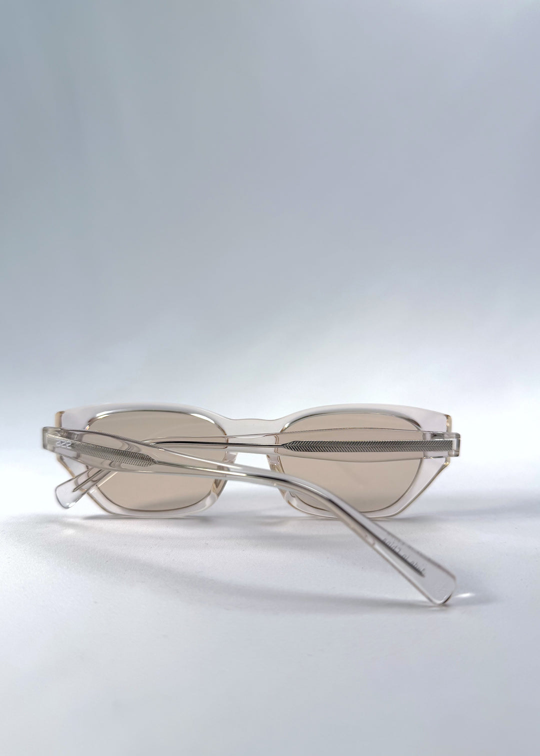 Folded view of Mirach sunglasses in Transparent White, featuring crystal-clear acetate frame and tea-tinted lenses, showing the folded temples and frame profile.