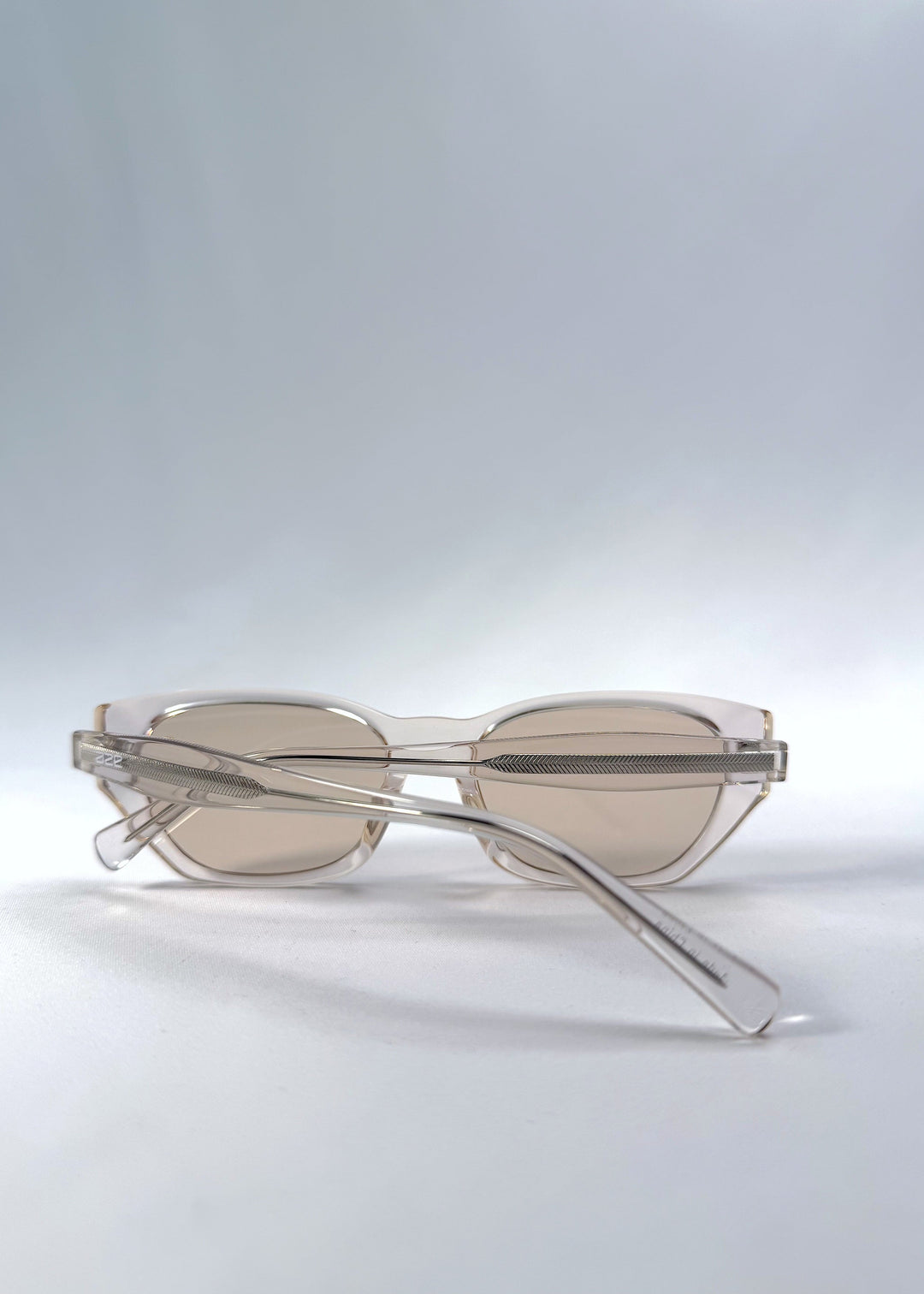 Folded view of Mirach sunglasses in Transparent White, featuring a crystal-clear acetate frame and tea-tinted lenses, showing the folded temples and frame profile. 