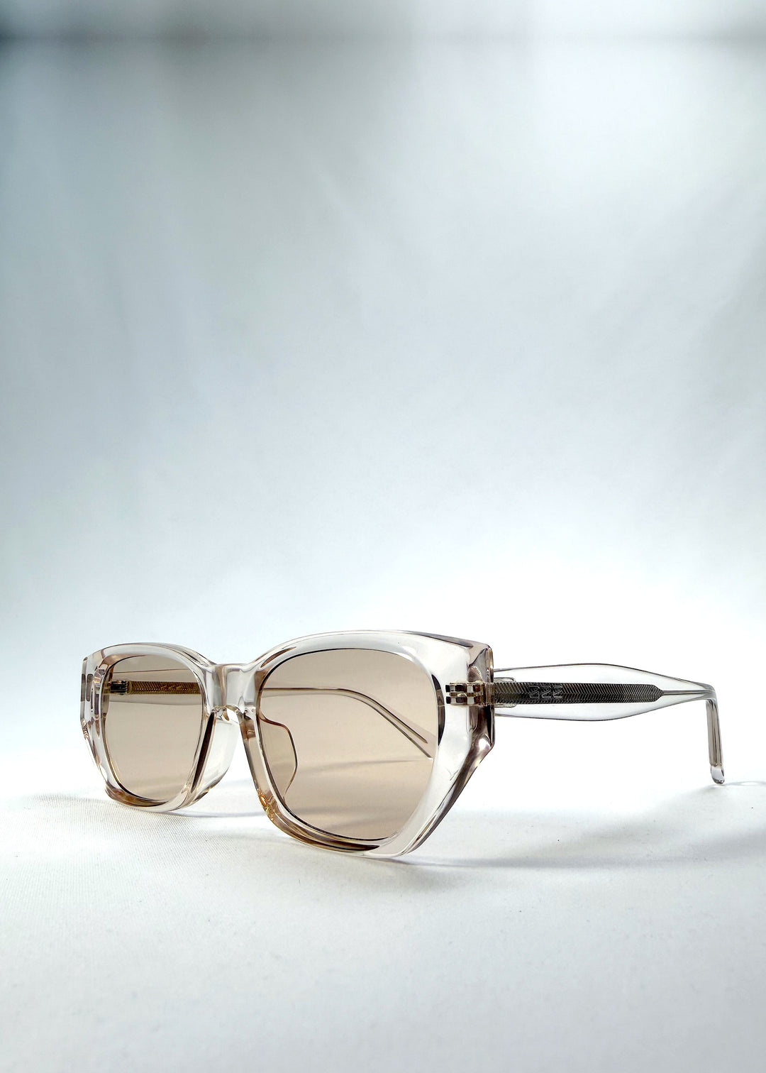 Three-quarter front view of Mirach sunglasses in Transparent White, featuring crystal-clear acetate frame and tea-tinted lenses, showing the front shape and temple profile.