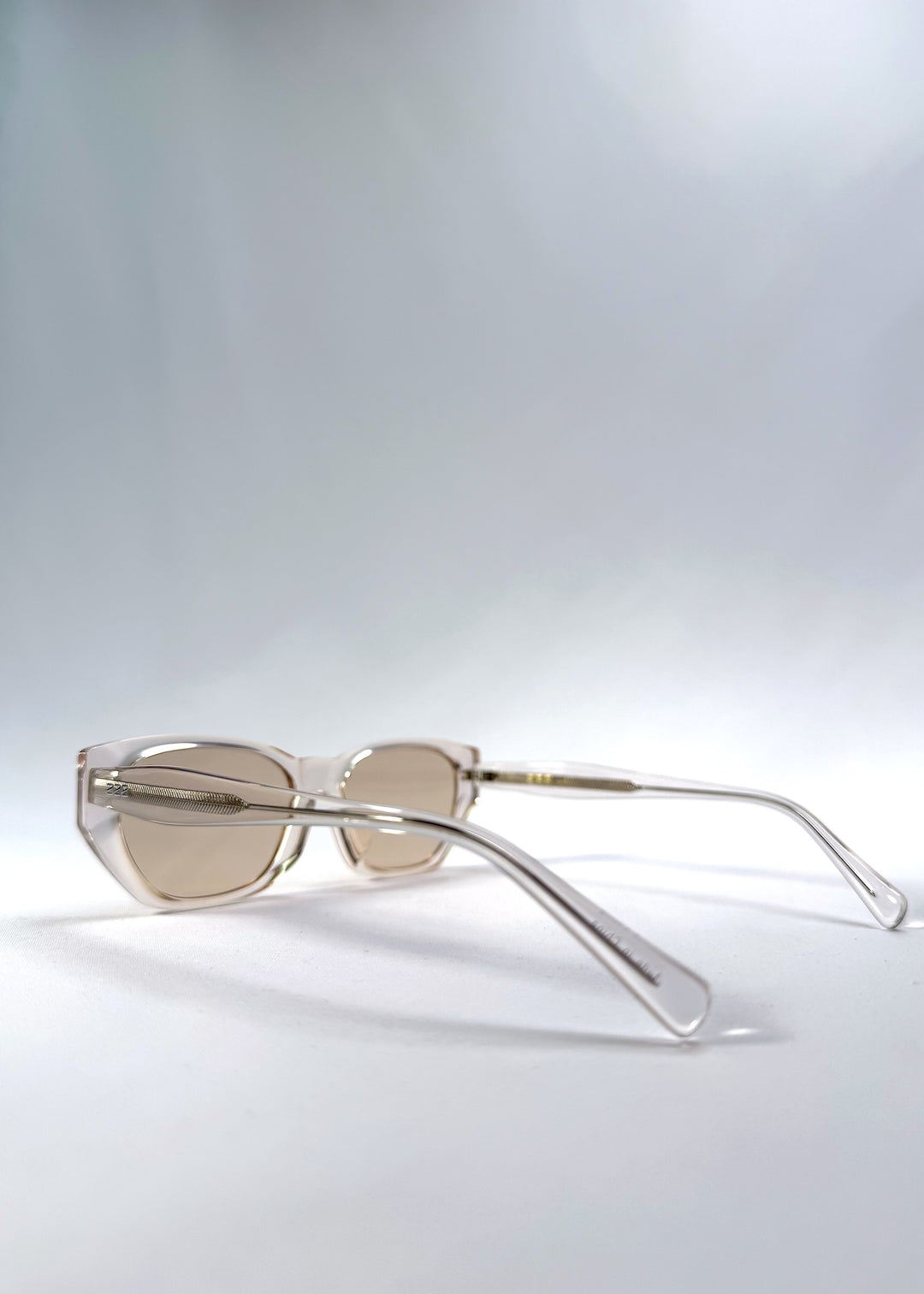 Side-angle view of Mirach sunglasses in Transparent White, featuring crystal-clear acetate frame and tea-tinted lenses, showing the lens shape and temple profile.