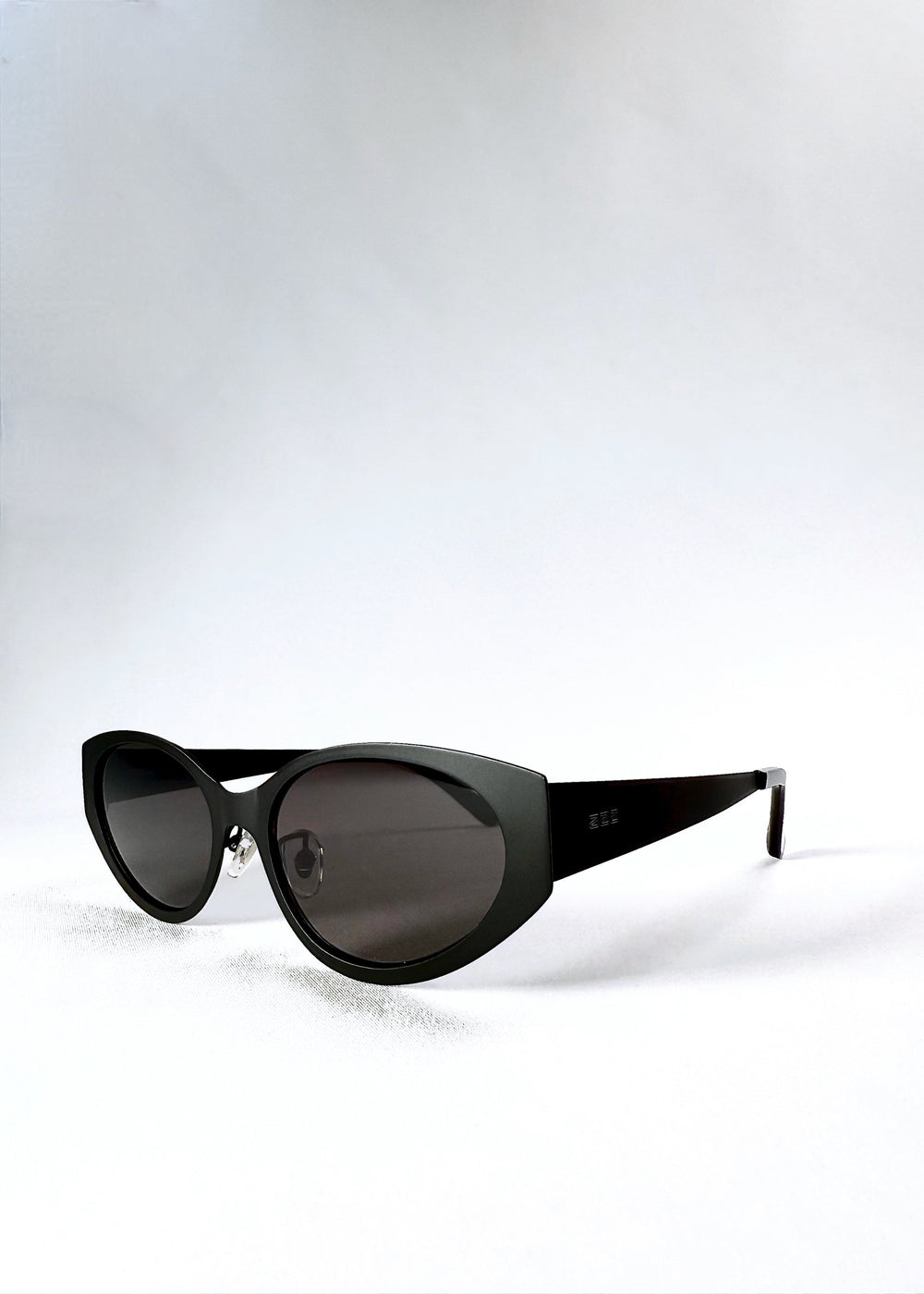 Three-quarter front view of Nyx sunglasses in Shadow Black, highlighting the tapered cat-eye frame and dark lenses.