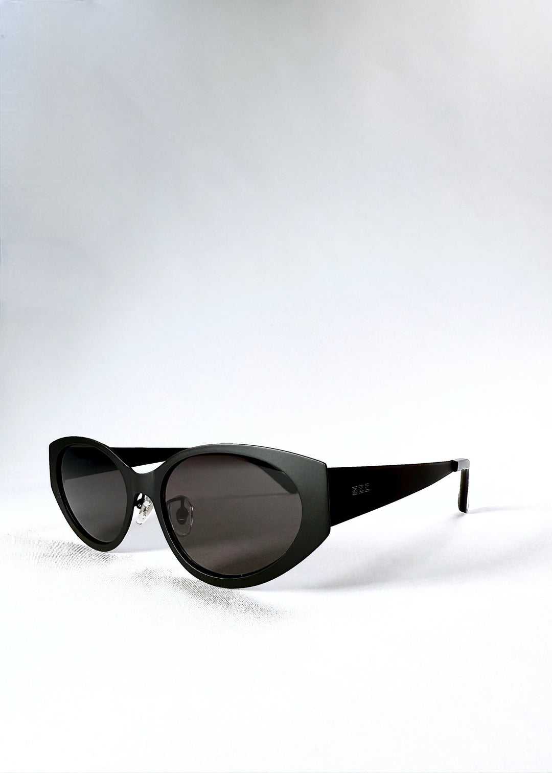 Three-quarter front view of Nyx sunglasses in Shadow Black, highlighting the tapered cat-eye frame and dark lenses. 