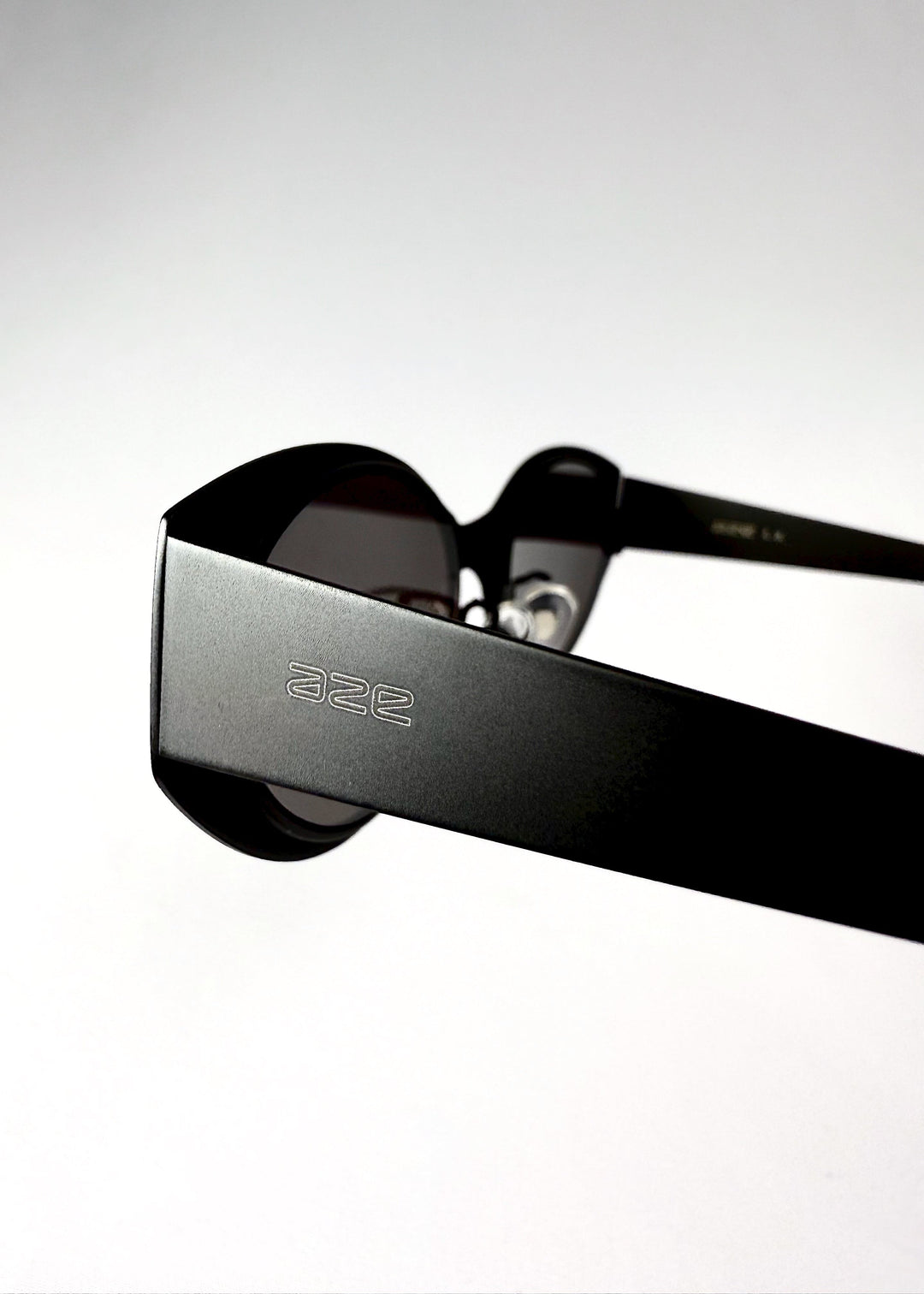 Close-up of the temple arm and engraved AZE logo on Nyx sunglasses in Shadow Black. 