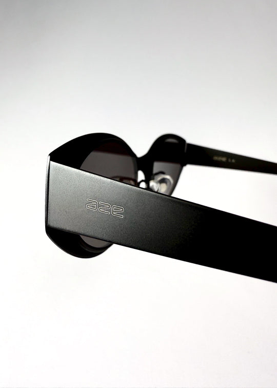 Close-up of the temple arm and engraved AZE logo on Nyx sunglasses in Shadow Black. 