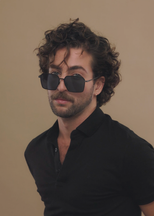 Male model wearing Rigel sunglasses in Blue Graphite with a dark polo, head turned to the side. 