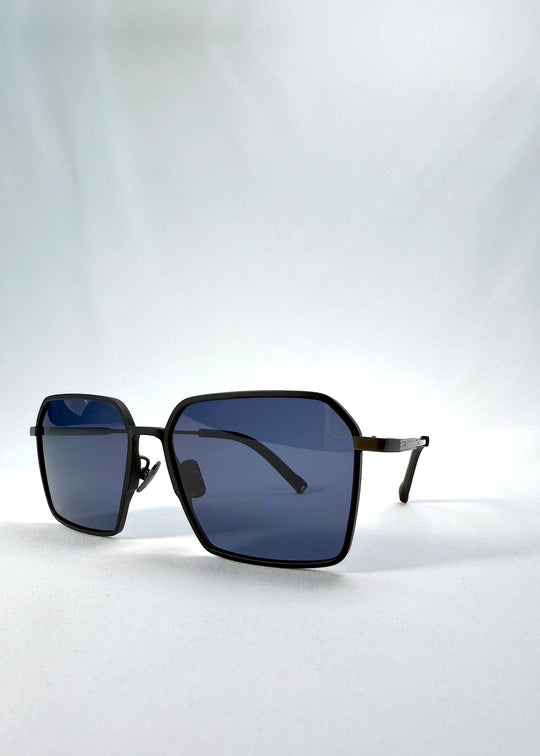 Three-quarter front view of Rigel sunglasses in Blue Graphite, featuring an ultra-light frame with titanium temples, geometric lens shape, and polarized lenses, showing the front shape and temple profile. 